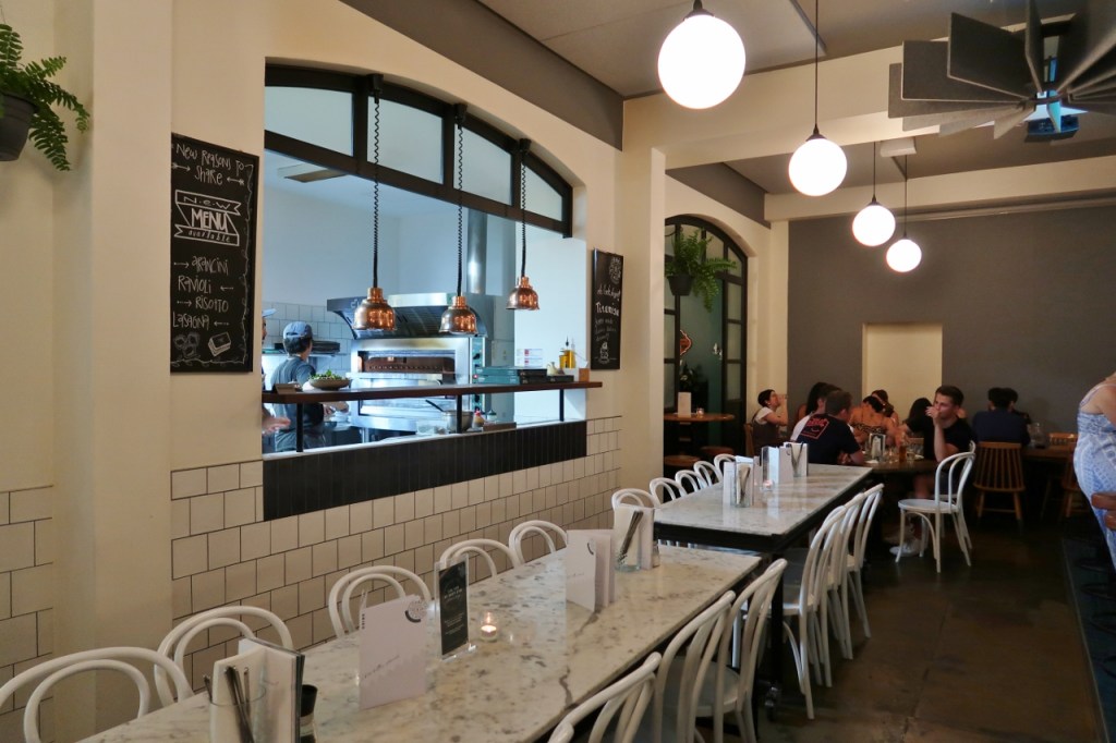 Seating area and a window opening into the kitchen at Corbett & Claude Restaurant