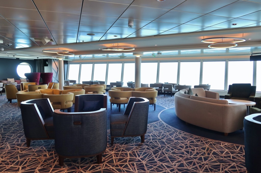 Lounge with sofas and armchairs overlooking the Palace swimming pool on Genting Dream Cruises