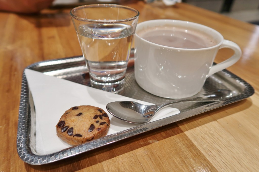 A small tray of hot chocolate, a cookie and a glass of water